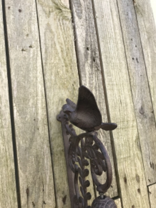 Eine verschnörkelte Türklingel mit einem Vogel darauf, aus Gusseisen
