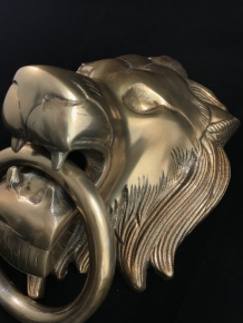 A lion's head, made of aluminum in a brass color, as a door knocker